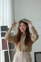 A young woman stands with a pen and a notebook on her head. Standing happily smiling in the office....