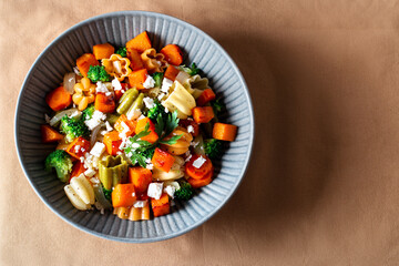 Autumn pasta salad with roasted pumpkin, broccoli, feta cheese on dark wooden background, fall season salad