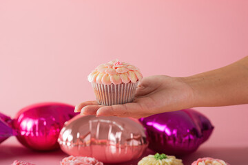 Female hand showing a cupcake in foreground. Pink background.