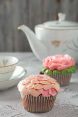 Colorful cupcakes with flower decorations made with butter cream, cup and teapot on the side.