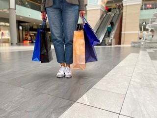 Unrecognizable female wearing jeans pants carrying in hands many shopping bags full of purchase....