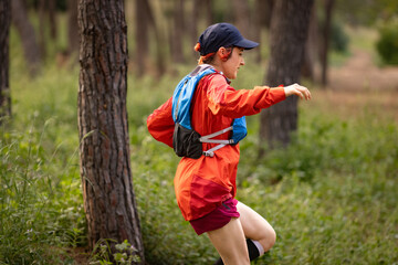 A woman in a red jacket and blue backpack is running through a forest. Concept of adventure and...