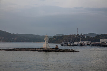 A beautiful lighthouse stands in the sea. Ships in the background. Clouds in the sky. Evening at sea.