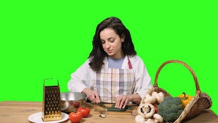 Pretty young woman slicing cucumber on a cutting board on the chroma key