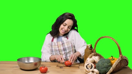 Pretty woman slicing tomato and talking on mobile phone on the chroma key