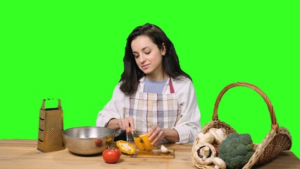 Smiling young woman slicing yellow pepper on a cutting board on the chroma key