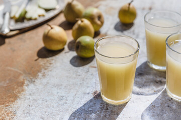 Pear juice in glasses surrounded by fresh fruits on strong sunlight