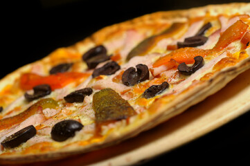 Pizza with ham, tomato and olives on a black background