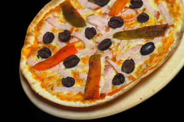 Pizza with ham, tomato and olives on a black background