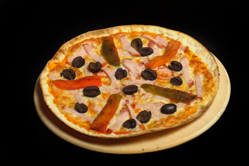 Pizza with ham, tomato and olives on a black background
