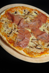 Pizza with ham, mushrooms and cheese on a wooden plate.