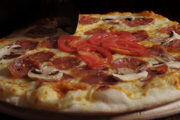 process of cutting pizza with ham, cheese and tomatoes on a wooden board.