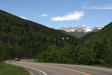 a car on a road with mountains in the background and trees to side