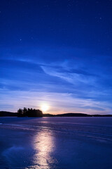 Fototapeta premium Serene nighttime winter landscape with a frozen lake and a glowing full moon in the blue sky