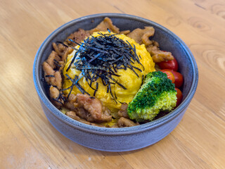 Teriyaki pork rice bowl with omelet and vegetable served on the table. Grilled pork and omelet in Japanese-style donburi.
