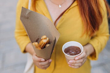 Woman eating traditional Churros, a fried pastry with chocolate on a city street. Food concept