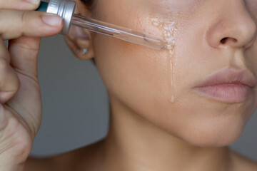 Cropped shot of a young woman applying anti-wrinkle serum to the skin on cheek with a dropper on...