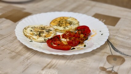 Round fried eggs with tomatoes on a white plate on a tablecloth. Close-up