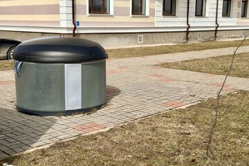 A round grey dumpster for the disposal of food waste is located next to an apartment building....