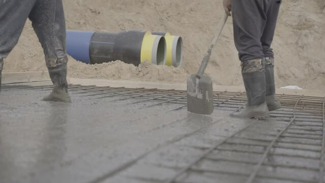 Male workers level mortar in formwork at construction site. Men with shovels pour concrete mortar onto network of rebar slow motion