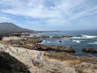Foamy waves of an ocean hitting the rocks on the shore with the horizon in the sunny background