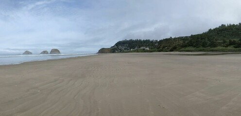 Sandy beach and the calm waters of the sea with the horizon and a cloudy sky in the background
