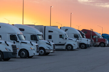 Line of Parked Semi-Trucks Bathed in Warm Sunset Light at a Rest Stop, Symbolizing Long-Haul Travel.