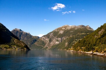 Scenic shot of a lake surrounded by green-covered hills under the blue sky