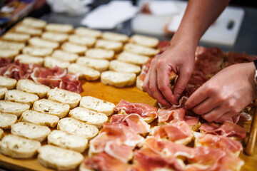 Preparation of canapes for celebration event. Female hands putting Parma ham on a sliced baguette. Food styling