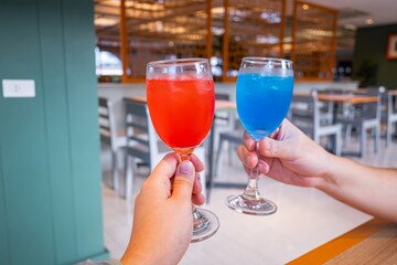 Two people are holding glasses of blue and red drinks