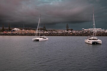 Boats are tied up at a dock in a body of water with a dark and foreboding sky in the background