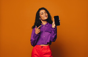 Vibrant woman recommending modern mobile device on orange background