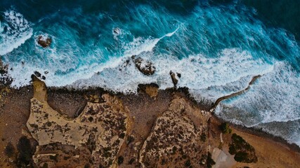 Aerial view of a coastal beach featuring picturesque waves crashing against rugged rocks and cliffs