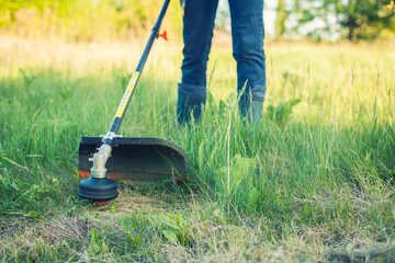 worker mows green grass on the lawn with hand trimmer. lawn care. weed control. Woman with gasoline...