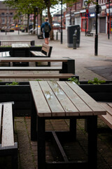 benches in the park. A picturesque street featuring tables and benches, green trees, street lamps, and shops. Perfect