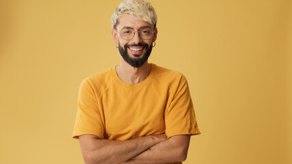Guy with glasses, dressed in yellow T-shirt, crossing arms and smiling looking at camera isolated...