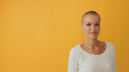 Young hairless woman looking at camera with smile, advertising space, isolated on yellow background...