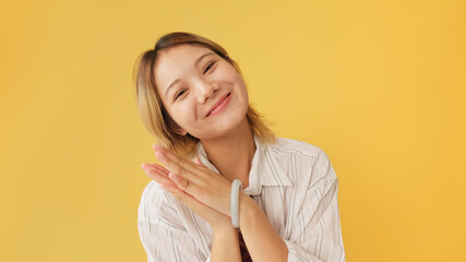 Surprised young woman dressed in shirt and tie covers her mouth with her hand and claps her hands isolated on yellow background in studio