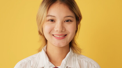 Close-up, woman opens eyes and looks at camera with smile isolated on yellow background in studio