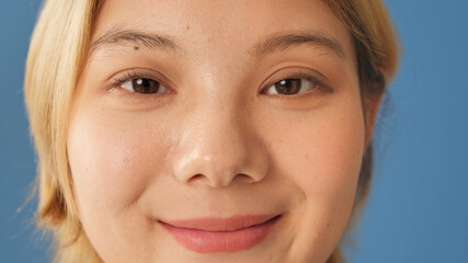 Close-up portrait of smiling woman looks at camera isolated on blue background in studio