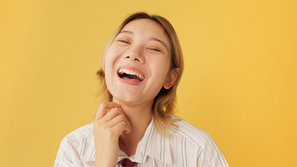 Young woman dressed in shirt and tie laughing while looking at camera isolated on yellow background...