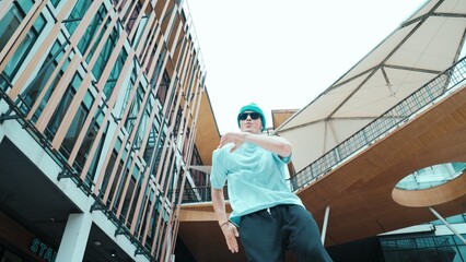 Portrait of caucasian street dancer looking at camera. Young attractive man moving, dancing practicing hip hop performance at modern mall. Low angle. Freestyle dance. Outdoor sport 2024. Endeavor.