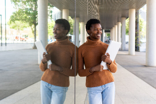 Confident student with laptop standing near glass wall