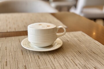 A coffee cup is placed on a saucer, resting on a wooden table. The tableware includes dishware and...
