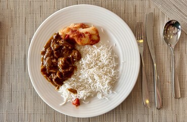 A plate of white rice and meat served on a table. The meal is a staple food in many cuisines and is...