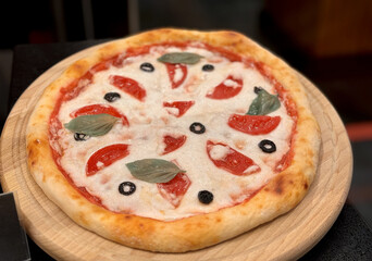 Top view of delicious sliced pizza with cheese and tomatoes on wooden dish on the table at the restaurant. Close-up