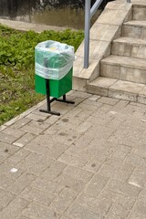 A green waste container is placed on the sidewalk next to stairs. The road surface is asphalt with grass and groundcover surrounding the area