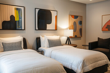 Chic hotel room, two single beds, modern art pieces, cozy sofa set, black chair, and trendy lamp. Comfortable and stylish.