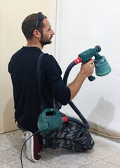 Man painting interior wall with sprayer in home during daytime