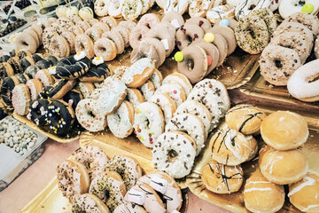 Sugary fried dough confections line rows at a street market - glazed, powdered, frosted, filled donuts galore. Plump classic rings ooze with vibrant fillings. A mouthwatering vista.
